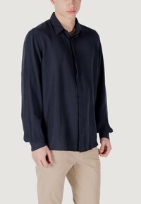 Marineblauwe overhemd met lange mouwen, gemaakt van een gladde stof, heeft een klassiek kraag en een ontspannen pasvorm. Gepaard met beige broeken.