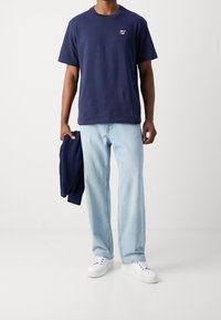 Marineblå bomulds t-shirt med et lille rødt logo på brystet, parret med lyseblå denimjeans og hvide snørebåndssneakers.