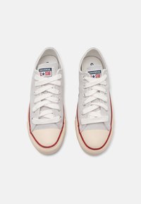 Adidași gri din pânză cu șireturi albe, accente roșii și vârf din cauciuc. Au un patch cu logo-ul "Converse All Star" pe limbă.