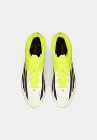 Φωτεινά κίτρινα ποδοσφαιρικά παπούτσια με κομψό σχεδιασμό, με μαύρες ρίγες, υφή στην επιφάνεια και αντίθετες κόκκινες λεπτομέρειες.