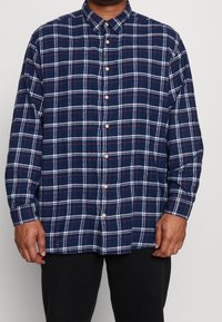 Camicia a quadri navy con bottoni, realizzata in tessuto morbido con motivi a griglia bianchi e rossi, dotata di maniche lunghe e polsini abbottonati.
