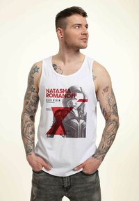 Hvid tanktop med et grafisk design af karakteren "Natasha Romanoff," med røde accenter og tekst, på en enkel baggrund.