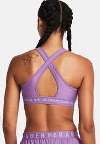 Lilla idretts-bh med racerback-design. Har en krysset båndstruktur på ryggen og logodetaljer på båndet. Myk, elastisk stoff.