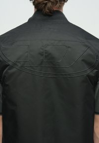 Schwarze Bomberjacke aus Satin mit großem, tonalem Stickdesign auf der Rückseite. Gerippter Kragen und Ärmel, glatte Textur und entspannte Passform.