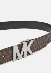 Rudas raštuotas audinio diržas su juodu odiniu pagrindu, kuris turi blizgų sidabrinį MK logotipo sagtį.