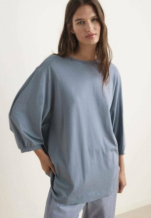 Light blue oversized t-shirt made from soft fabric, featuring a round neckline and loose three-quarter sleeves with elastic cuffs.