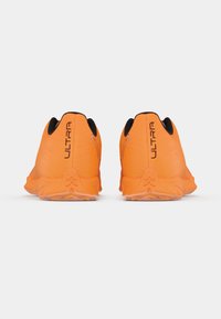 Scarpe da corsa arancioni con tomaia flessibile e strutturata, dettagli neri e suola robusta con motivi antiscivolo. Il marchio "ULTRA" è visibile.