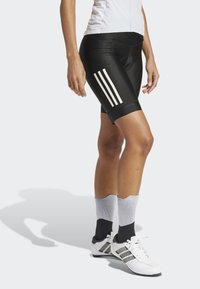 Black cycling shorts made of smooth fabric, featuring white three-stripe design on the side. Paired with white shoes and gray athletic socks.