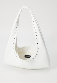 Sac synthétique blanc à forme arrondie, avec des clous argentés le long du bord et une ouverture sur le dessus, montrant une doublure intérieure simple.
