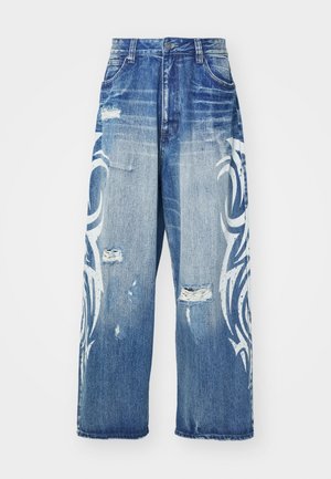 Šviesiai mėlyni plačių kojų džinsai su nublukusiu apdaila, turintys baltus tribalinio stiliaus raštus ir nusidėvėjimo detales priekyje.