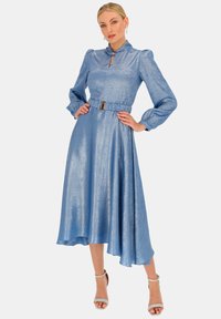 Niebieska, metaliczna sukienka z długim rękawem, wysokim kołnierzem, plisowanym pasem i asymetrycznym dołem. Posiada akcent w postaci złotej tonowanej paska.