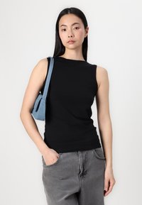 Black sleeveless top with a fitted design, made from smooth fabric. Paired with gray denim pants and a small blue denim bag.