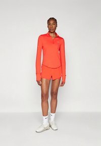 Červený športový komplet s dlhým rukávom a krátkymi nohavicami s reflexným logom Nike. Texturovaná látka, zips na golieri a priliehavý strih. Tenisky a biele ponožky.