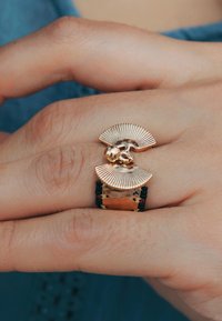 Bague dorée avec deux accents en forme de ventilateur et un détail sphérique central, avec des éléments noirs et métalliques intégrés dans la bande.