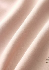 Miękka różowa tkanina o delikatnej strukturze splotu i łagodnych fałdach, ukazująca gładkie, lekko wypukłe detale powierzchni.