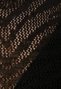 Tessuto in maglia nera con un motivo in pizzo, caratterizzato da fori di diverse dimensioni. Aspetto texturizzato e leggero con una finitura liscia.