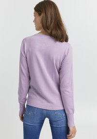 Pulover lung cu mânecă lilac, fabricat dintr-un material moale, cu decolteu rotund și manșete cu nervuri, asortat cu blugi din denim albastru.