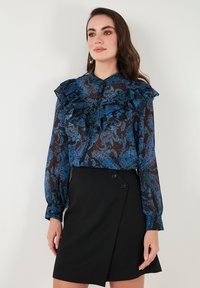 Sheer blue patterned blouse with ruffled collar and cuffs, paired with a black wrap skirt featuring double button detail.