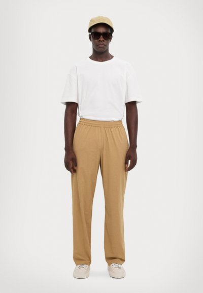 Hvit kortermet skjorte, beige elastisk bukse, beige cap, svarte solbriller, kremfargede sneakers. Enkel, avslappet passform, minimalistisk design.