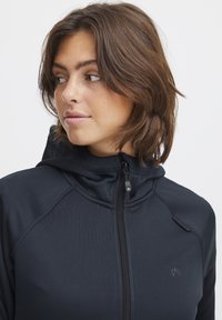 Felpa nera con zip realizzata in tessuto liscio, dotata di collo alto, cappuccio regolabile con cordino e logo sul petto.