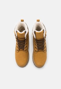 Bottines couleur fauve avec une tige lisse, un col doublé de fourrure et des lacets contrastants. Semelle en caoutchouc texturée et détail de languette avec logo.