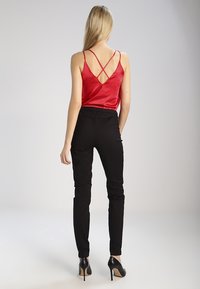 Röd satin cami med korsade ryggband, tillsammans med svarta åtsittande byxor och svarta klackar, som visar en smal silhuett och mjuka texturer.