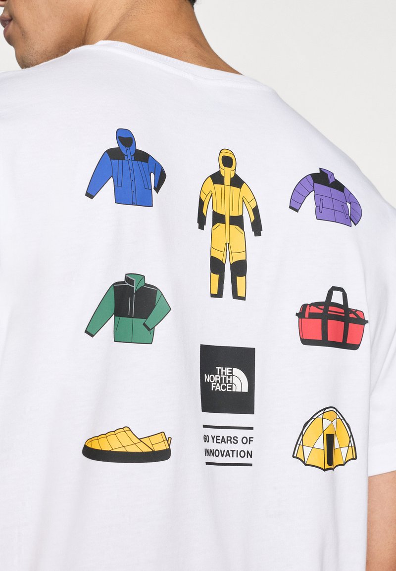 T-shirt blanc avec des motifs graphiques colorés présentant divers vêtements d'extérieur, sacs et une tente, étiquetés avec le logo "The North Face".