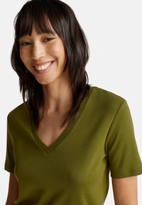 Olivenfarbene kurzärmelige V-Ausschnitt-T-Shirt aus weichem, leichtem Material. Verfügt über eine figurbetonte Form und eine glatte Textur mit einem schlichten Design.