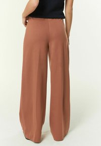 Pantaloni largi de culoare teracotă, confecționați dintr-un material neted. Prezintă un talie înaltă și un drapaj fluid pentru o potrivire lejeră.