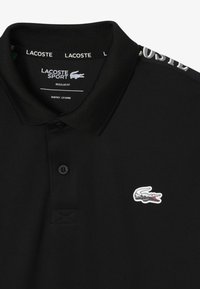 Polo shirt nero, vestibilità regolare, con un tessuto testurizzato. Presenta un colletto con il marchio e un piccolo logo colorato sul petto. Due bottoni al collo.