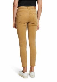 Skinny jeans in tan cotton blend with a high waist, featuring two back pockets and stitched detailing. Paired with white sneakers.