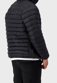 Giacca a sacco nera con design trapuntato, caratterizzata da cuciture orizzontali, un colletto alto e chiusura con zip. Materiale morbido e testurizzato.