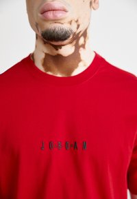 Piros póló kerek nyakkivágással és fekete hímzett "JORDAN" logóval. Simára szőtt anyag és kényelmes szabás.