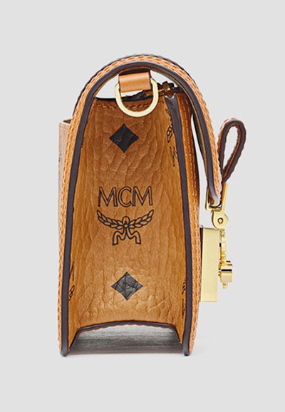 Brunt tekstureret læder MCM taske set fra siden med sorte logoer, guldhardware og stikninger på en ensfarvet lys baggrund.