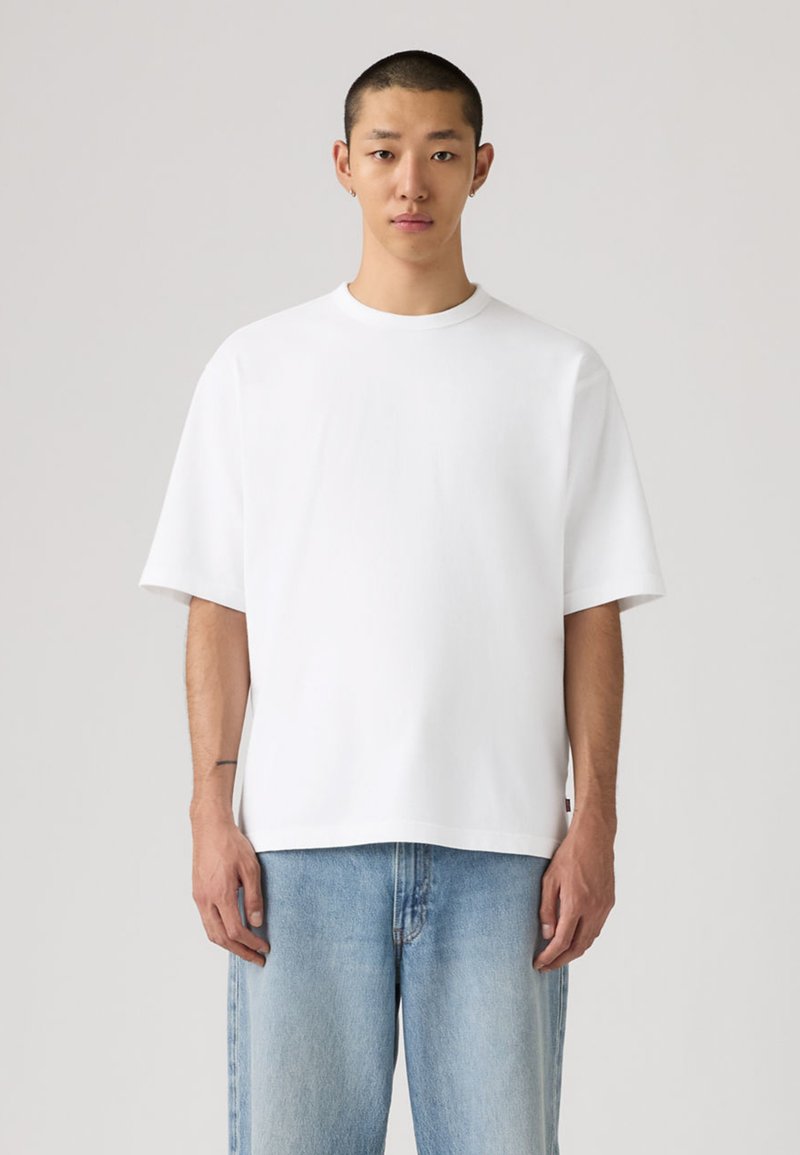 T-shirt en coton blanc à coupe décontractée, col rond et manches courtes, associé à un pantalon en denim bleu clair. Design simple, sans motifs.