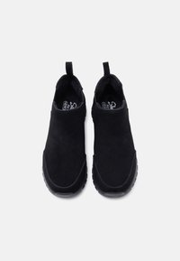 Ζευγάρι μαύρα παπούτσια χωρίς κορδόνια με επάνω μέρος από σουέντ και λαστιχένιες σόλες, σε θέα από πάνω σε απλό ανοιχτό φόντο.