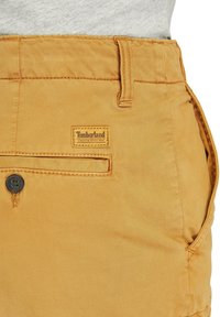 Timberland-shorts i orangebrunt bomullsmaterial, med en knappad framficka, synlig sömnad och en logotyp på midjebandet.
