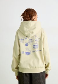 Sweatshirt creme com capuz, de corte descontraído e punhos canelados. Apresenta desenhos em linha azul de copos e a frase "TIRE O SEU TEMPO" nas costas.