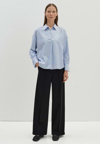 Camicia azzurro chiaro a maniche lunghe con colletto, apertura frontale e vestibilità rilassata, abbinata a pantaloni larghi neri e scarpe nere.