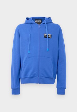 Modrá mikina na zip vyrobená z bavlněné směsi. Obsahuje přední kapsu a nastavitelnou kapuci na šňůrku. Černý logo nášivka na hrudi. Měkká textura.