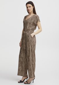 Jumpsuit a stampa leopardata in morbido tessuto, con maniche corte, scollo a V, vita annodata e silhouette a gamba larga con tasche laterali. Tacchi neri.