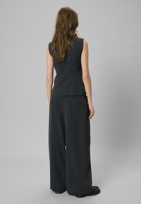 Sötétszürke, testhezálló, ujjatlan felső széles lábú nadrággal párosítva, függőleges csíkokkal és sima anyagú kivitelezéssel.