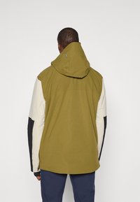 Hupparitakki oliivinvihreänä, jossa on kerma- ja musta värilohkottu hiha. Valmistettu pehmeästä, teksturoidusta kankaasta joissa on säädettävä huppu ja sivu-zip.