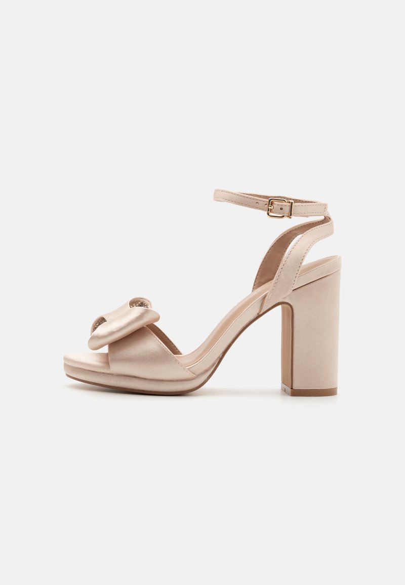 Beige satin högklackad sandalett med en ankelsnodd och en dekorativ rosett på tån. Har en kraftig häl och en slät yta.