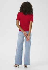 Rotes, geripptes T-Shirt mit kurzen Ärmeln, kombiniert mit hellblauen, weit geschnittenen Jeans und beigen hohen Schuhen, von hinten betrachtet.