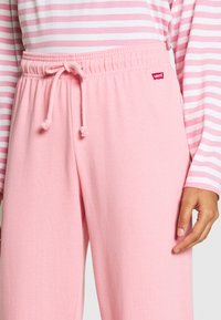 Light pink sweatpants with an elastic waistband and drawstring; features a Levi's logo tag; paired with a pink and white striped top.