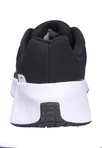 Scarpa atletica nera con tomaia in tessuto testurizzato, tacco imbottito e suola in gomma bianca. Presenta un logo discreto e accenti a contrasto.