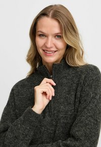 Maglione pullover grigio scuro con zip, realizzato in un morbido tessuto a maglia texture. Presenta un colletto alto e polsini a coste. Design semplice e funzionale.