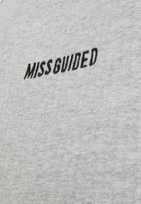 Tessuto in cotone grigio con una morbida texture, caratterizzato dal nome del brand ricamato "MISSGUIDED" in lettere nere in grassetto.
