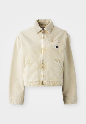 Veste courte beige en tissu doux, dotée d'une fermeture éclair frontale, d'un col, de deux poches latérales et d'un petit logo cousu sur la poitrine.